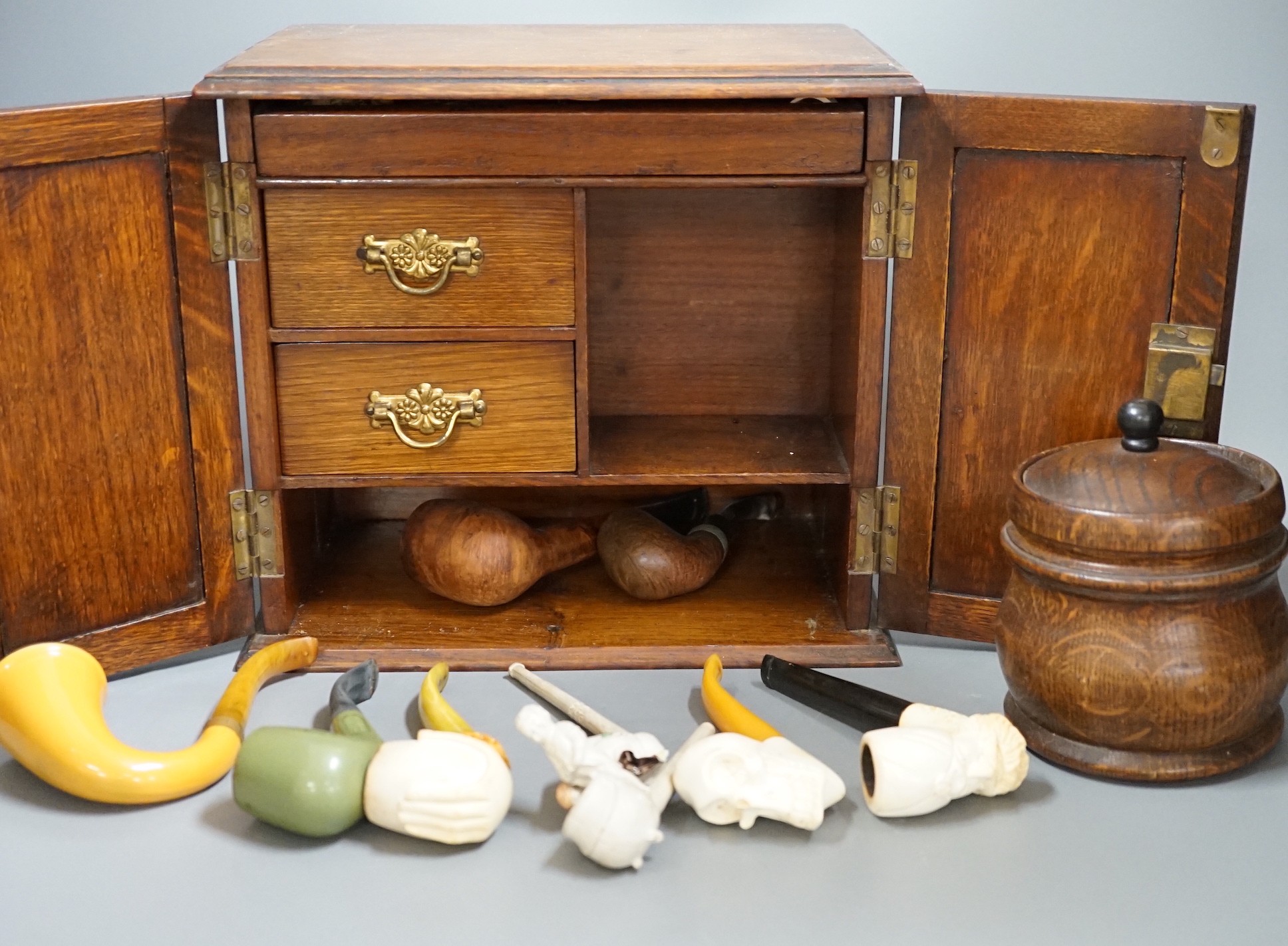 A carved smoker’s cabinet containing Meerschaum and other pipes and a tobacco jar, cabinet 25cm high